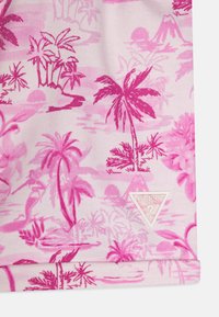 Rosa stof med tropiske palme- og ømønstre, med et hvidt trekantet logotag, der læser "GUESS® USA" nederst til højre.
