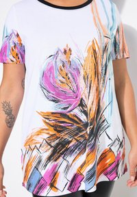 Top corto de manga corta blanco con un diseño floral abstracto en púrpura, naranja y negro, con un escote negro y una silueta fluida.