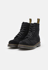 Black suede ankle boots with gray laces, yellow pull tab, and yellow stitching on a thick black sole. Classic lace-up design.
