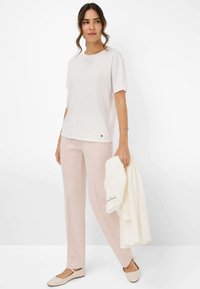 Kurzes weißes Oberteil mit kurzen Ärmeln, leichte rosa gemusterte Hose und beigem Ballerinas. Hält einen cremefarbenen Schal. Minimalistischer Stil, neutrale Farben.