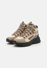 Beige and gray hiking shoes with green and burgundy accents, featuring a textured rubber sole, layered design, and metal eyelets for laces.