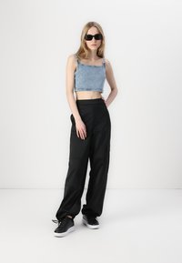 Denim crop top s tankovima, u kombinaciji s crnim, širom cargo hlačama. Crne tenisice upotpunjuju outfit. Minimalistički ambijent.