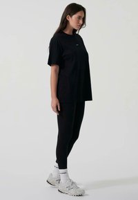 Svart oversized t-shirt med korta ärmar och rund halsringning, kombinerad med svarta leggings. Modellen har på sig grå sneakers med vita strumpor.