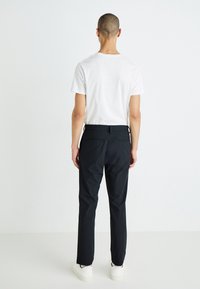 Pantalons noirs avec une coupe droite, présentant une texture lisse et des passants de ceinture, associés à un t-shirt blanc uni et des baskets blanches.