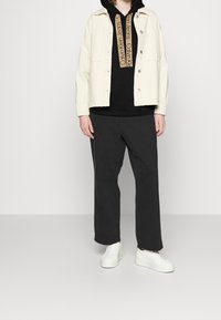 Biała kurtka dżinsowa na czarnej bluzie z kapturem z beżowym logo, w połączeniu z czarnymi spodniami o szerokich nogawkach i białymi trampkami. Prosty i nowoczesny design.