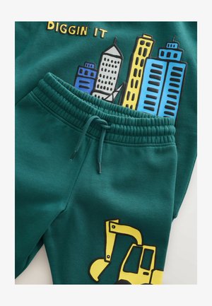 Completo felpa e pantaloni verdi. Presenta una grafica gialla di un escavatore e un design dello skyline della città in blu e grigio. Tessuto morbido e strutturato con vita elastica.