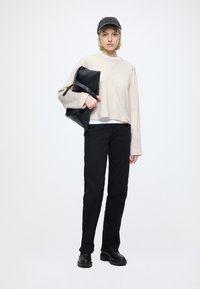Pull crème, pantalon noir et chaussures noires. Porte un sac noir avec une bandoulière. Design simple, coupe décontractée et palette de couleurs minimaliste.