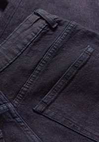 Donkerdenim stof met een gladde textuur, voorzien van een voorzak, riemlus en contrasterende stikdetails.