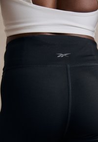 Czarne legginsy o wysokim stanie wykonane z elastycznej tkaniny o gładkiej strukturze. Posiadają logo na tylnym pasie oraz płaskie szwy.