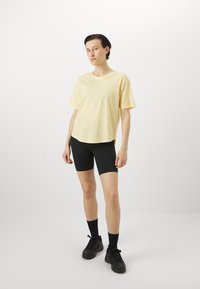 Lysegul bomull T-skjorte med korte ermer, rund hals og sidesplitter. Kombinert med svarte sykkelshorts og svarte joggesko.