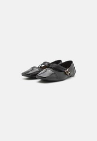 Schwarze flache Schuhe mit einer spitzen Zehenpartie, glänzender Oberfläche, Kreuzriemen und einer goldfarbenen Schnalle an der Seite.