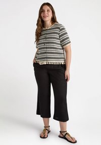 Czarny i biały pasiasty sweter dzianinowy z pomponowymi wykończeniami, w zestawie z luźnymi czarnymi spodniami w 3/4 i płaskimi sandałami z ozdobnym akcentem.