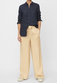 Persona che indossa una camicia blu navy con le maniche arrotolate e pantaloni beige larghi con cordoncino alla vita, abbinati a sneaker bianche.