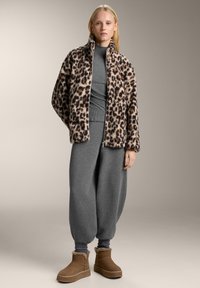 Giacca in pile con stampa leopardata e colletto alto, abbinata a un maglione grigio e pantaloni sportivi grigi larghi. Stivaletti alla caviglia foderati in pelliccia marrone.