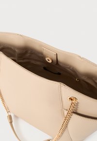 Μπεζ τσάντα χειρός από τεχνητό δέρμα με χρυσή αλυσίδα λουρί, διαθέτει κλείσιμο με μαγνητικό κούμπωμα και λείο, υφή με υφή. Το εσωτερικό είναι επενδυμένο και ευρύχωρο.