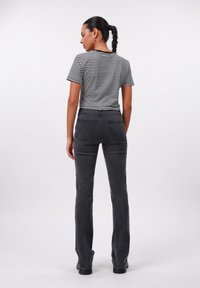 Moteris su pintu uodegos kuodu, dėvinti juodai baltą dryžuotą trumpą rankovę marškinėlį, tamsiai pilkus aukštai iškeltus džinsus, stovi atsisukusi atgal.