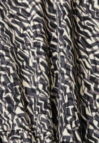 Motif géométrique en zigzag noir, blanc et gris sur tissu froncé, créant un effet texturé et ondulé.