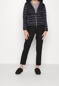 Foret navy jakke med hætte, lynlås og ribstrikkede manchetter, kombineret med sorte bukser og polstrede sorte slip-on sko.