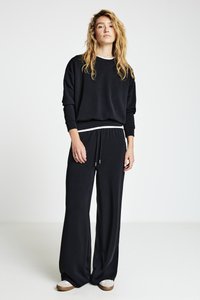 Sweat-shirt noir et pantalon à jambes larges en tissu doux, avec un accent blanc sur les poignets et la taille. Stylé avec des chaussures décontractées.