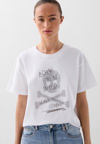 Witte katoenen t-shirt met een relaxte pasvorm, voorzien van een grijze skeletgrafiek en de tekst "BORN TO BE WILD" en "SCALPERS COMPANY." Korte mouwen.
