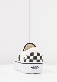 Vans slip-on tenisice imaju crno-bijeli karirani uzorak, gornji dio od tkanine, podstavljen ovratnik i bijelu gumenu potplatu s logotipom brenda.