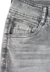Jeans in denim grigio con tasca frontale decorata con cuciture, rivetto in metallo e finitura sbiadita. Il tessuto ha una texture liscia.