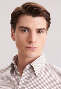 Camicia con colletto di un beige chiaro con un piccolo motivo a scacchi marrone. Tessuto liscio, con dettagli dei bottoni visibili sul davanti.