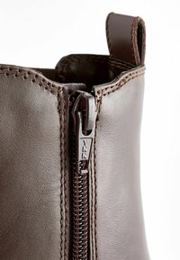 Bruna läderankelboots med en sidoglidare och brunt sömnad. Dragkedjan är märkt "YKK" för hållbar stängning.
