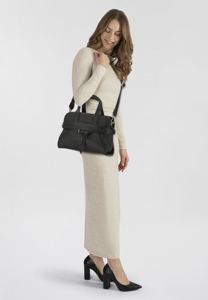 Zwarte leren handtas met gestructureerd ontwerp, korte handvatten bovenaan en een afneembare crossbody riem, gecombineerd met een aansluitende beige jurk met lange mouwen.