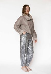 Grijze leren cropped jas met een pluizige kraag, gecombineerd met metallic zilverkleurige pantalons met slangenprint en lichtroze slippers.