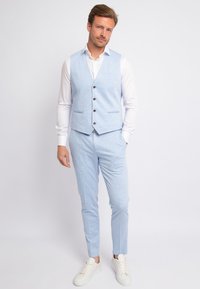 Hellblauer Anzug mit einer taillierten Weste und passenden Hosen. Der Stoff hat eine dezente Textur. Kombiniert mit einem weißen Hemd und weißen Sneakers.
