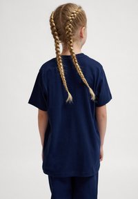 Mørkeblå bomulds t-shirt med korte ærmer, afslappet pasform og rund halsudskæring, vist fra ryggen med to fletninger.