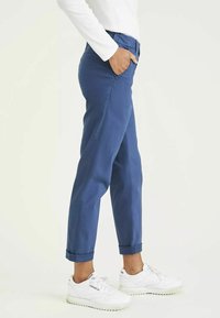 Pantalons en coton bleu avec une coupe slim, ourlets à revers, poches latérales et une texture lisse, accompagnés de chaussures de sport blanches.