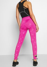 Leggings rosa con un motivo NIR sottile, vita alta e aperture alla caviglia. Abbinate a un top sportivo nero e scarpe nere.