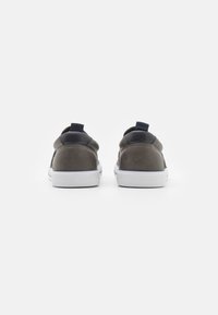 Baskets en suede grises avec accents en cuir noir, bout rond, semelle en caoutchouc blanche et tirette au niveau du talon. Design simple et profil bas.