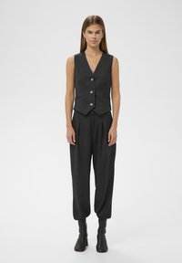 Chaleco entallado gris oscuro con cinco botones, combinado con pantalones grises de corte amplio. La tela tiene una textura suave. Botines negros hasta el tobillo completan el conjunto.