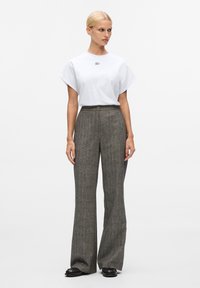 Tricou alb cu mânecă scurtă, cu un logo, asortat cu pantaloni gri în carouri, cu talie înaltă și picioare largi, și pantofi negri. Material neted cu linii curate.