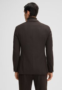 Bruine op maat gemaakte blazer met gestructureerde schouders en een hoge kraag, voorzien van een textuurstof en twee knopen op elke manchet.