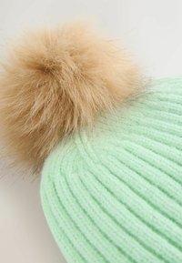 Strikket mintgrøn hue med ribbet tekstur og en stor kunstig pelskvast i en lys tan-farve.