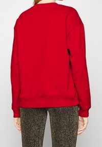 Sudadera roja con cuello y puños de punto acanalado, de corte holgado. Llevada sobre unos leggings dorados con textura brillante.