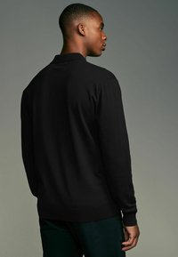 Schwarzes langärmeliges Polohemd mit geripptem Kragen und Bündchen, das über eine glatte Textur und eine figurbetonte Silhouette verfügt.