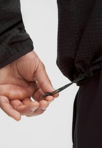 Sort udendørsjakke med tekstureret stof; håndjusterbar elastisk snøre med plastlås i kanten for en tætsiddende pasform.