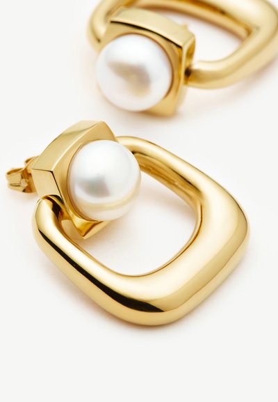 Χρυσά γεωμετρικά σκουλαρίκια κρίκοι με ένα μεγάλο λευκό μαργαριτάρι τοποθετημένο σε τετράγωνη χρυσή βάση σε κάθε ένα.