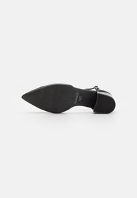 Zapato de tacón alto negro con punta afilada y suela texturizada, que presenta un diseño elegante. El material parece suave con una sutil marca.