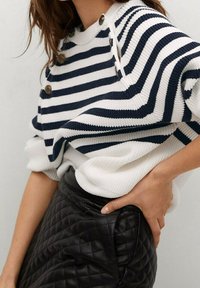 Gestreifter, gerippter Pullover in Marineblau und Weiß mit hohem Kragen, Knopfdetails an der Schulter, kombiniert mit einem schwarzen, gesteppte Lederrock.