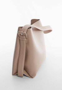 Stor, beige mulepose lavet af glat materiale, med en bred skulderrem med et rektangulært spænde og åben top.