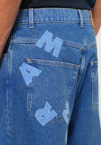 Jeans i denim i blått med ljusblå tygbokstäver "M A R" broderade på bakfickan. Har klassiska fickor och sömnadsdetaljer.