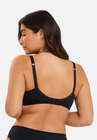 Soutien-gorge noir avec des bretelles réglables, un bord festonné et une fermeture à crochets au dos, fabriqué en tissu lisse et extensible.