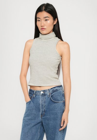 Top senza maniche a collo alto a righe in crema e nero, abbinato a jeans in denim blu a vita alta. Il tessuto appare liscio con un design aderente.