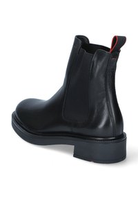 Stivale Chelsea in pelle nera con pannelli laterali elastici, superficie liscia, punta rotonda e una suola in gomma robusta. Accentazione rossa sul passante del tallone.